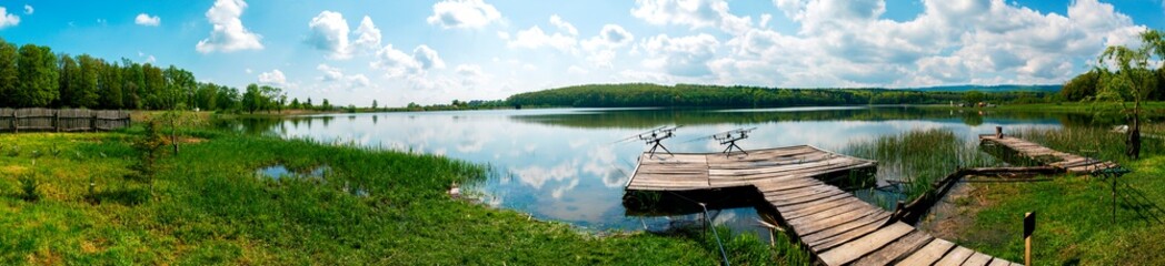 fishing pole with beautiful lake, mountains, forest and steel sky background. Fishing tool and sport concept