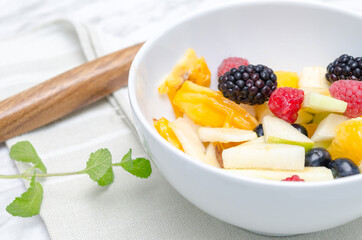 Fruit salad in white bowl. Wooden spoon background.