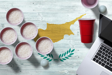 Cyprus flag concept with plastic beer pong cups and laptop on national wooden table, top view. Beer Pong game.