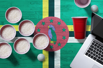 Dominica flag concept with plastic beer pong cups and laptop on national wooden table, top view....