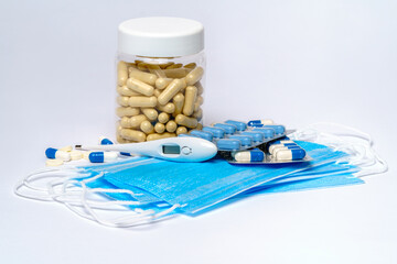 Disposable Medical protective mask with can of pills and thermometer over light grey background