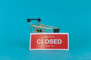 Red plate Sorry We're Closed COVID-19 with a supermarket trolley on blue background.