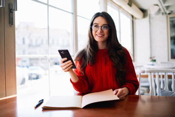 Cheerful talented female student of college surfing useful information on websites for upcoming seminar lesson on mobile phone,teen positive girl enjoying recreation time while messaging with friends