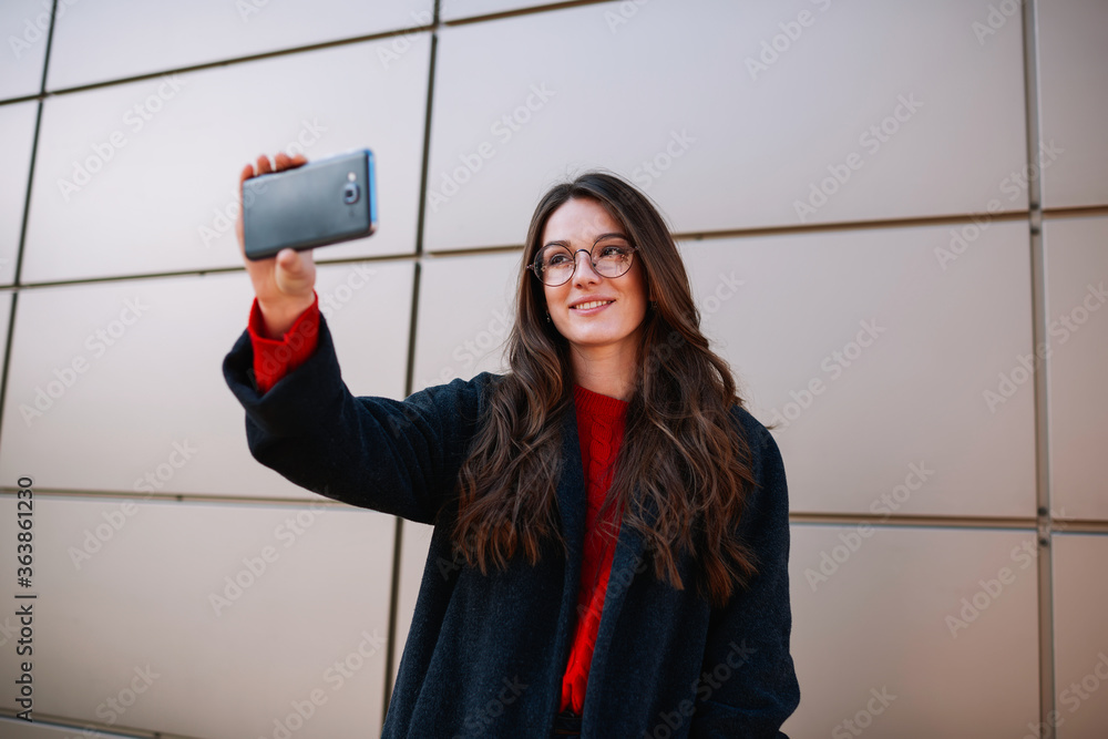 Poster good looking smiling hipster girl in spectacles streaming live video for friends using application a