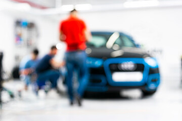 Fototapeta premium Blurred abstract image of man worker with car in a body shop. Blur car auto service. Car bokeh. Blurred background with car in garage. Vehicle maintenance in auto repair service. 