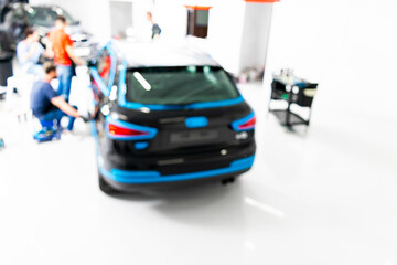 Blurred abstract image of man worker with car in body shop. Blur car auto service. Car bokeh. Blurred background with car in garage. Vehicle maintenance in auto repair service. Blurry service station