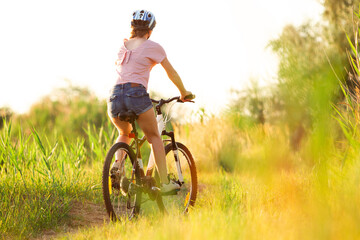 Mood. Joyful young woman riding a bicycle at the riverside and meadow promenade. Inspired by surrounded nature, summertime mood. Warm sunshine colors. Sport, activity, wellness, enjoyment concept.