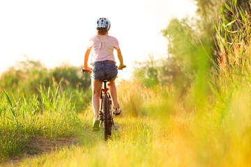 Mood. Joyful young woman riding a bicycle at the riverside and meadow promenade. Inspired by surrounded nature, summertime mood. Warm sunshine colors. Sport, activity, wellness, enjoyment concept.