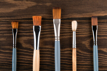 5 thin brushes lie on a wooden table: the artist prepared his tools for working on a new painting