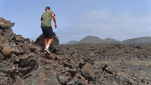 Hombre joven sube a la cima de una roca de lava para contemplar el paisaje volc&aacute;nico. Parque Nacional de Timanfaya. Lanzarote. Islas canarias