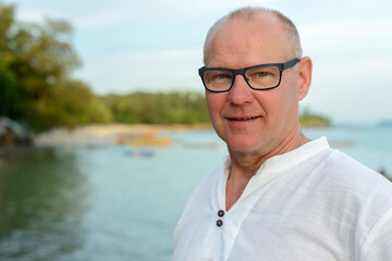 Happy mature handsome tourist man smiling against view of the beach outdoors