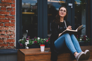 Thoughtful female writer pondering on new chapter for book about life sitting on bench with...