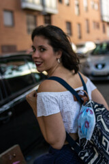 Photo of a young and attractive woman wearing a backpack with a disposable face mask attached to it with lipstick on it walking down the street