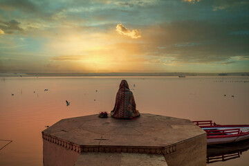 A person is watching beautiful sunrise on the bank of river ganga at ghats of varanasi while meditating - obrazy, fototapety, plakaty