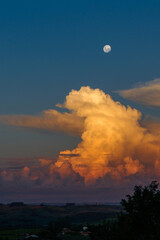 Fototapeta premium entardecer com lua cheia e nuvens iluminadas pelo por do sol