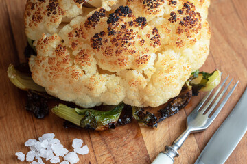 Whole grilled Cauliflower out of the oven with sea salt on a wooden board. Vegan food. Vegeterian food. Cooking at home. Close-up