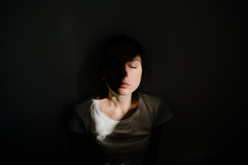 Girl sitting alone in sunlight pocket in dark room. mental health concept