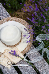 A straw hat, lice ribbons, vintage scissors and little lavender bouquet on wooden bench near...