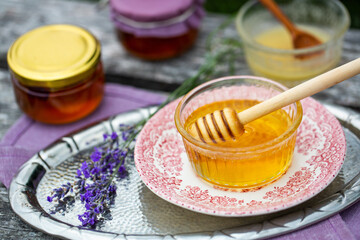 Two glass bowls with fresh natural lavender honey, jars with honey and lavender flowers on wooden background.