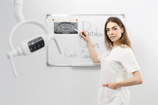 Young female dentist doctor standing in front of a white board examines an x-ray picture or writes something
