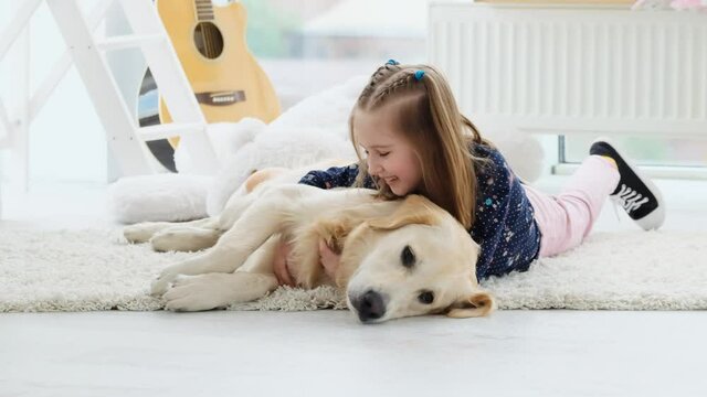 Cute little girl palming adorable dog lying on floor in light room