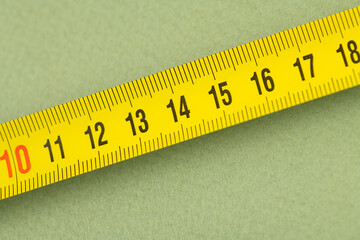 yellow construction measuring tape lies on a table, closeup photo 11 - 17 centimeters; green background
