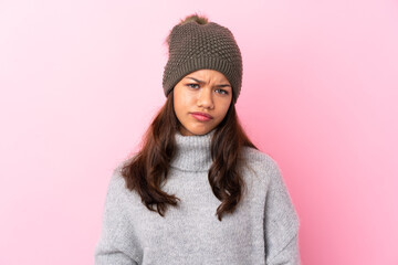 Young Colombian girl with winter hat over isolated pink wall sad