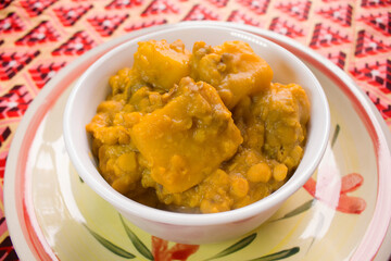 A white bowl of Yam and Beans Pottage or Nigerian Porridge served on a Plate with a colorful African 
 cream and red color pattern tablecloth 