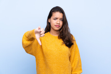 Young Colombian girl with sweater over isolated blue background showing thumb down with negative expression