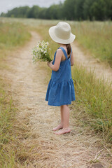 6 years old girl with bouquet of chamomiles looks away towards the horizon