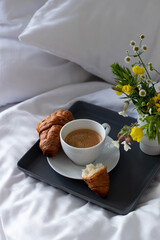 breakfast in bed, tray with cup of coffee, french croissant, in the morning, white bedding in the hotel room