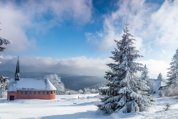 Red church and snow-covered trees on mountain against thick clouds in distance