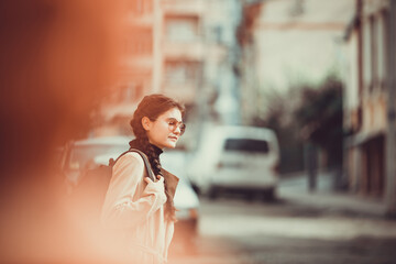 Retro style shot of young girl hitchhiking on the road in new city. Focus on girl, forefront and background are blurred.