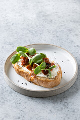 One sandwich with radish microgreens and sun-dried tomatoes on grey. Vertical.