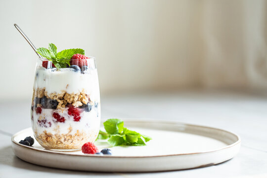 Glass of parfait made of granola, berries and yogurt on the table. Shot at angle with place for text, selective focus.