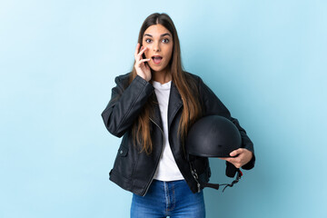 Young caucasian woman holding a motorcycle helmet isolated on blue background with surprise and...