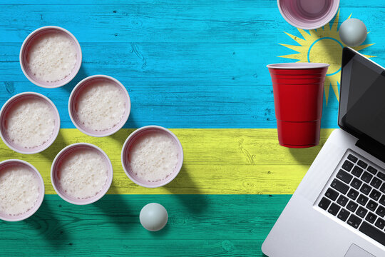 Rwanda flag concept with plastic beer pong cups and laptop on national wooden table, top view. Beer Pong game. - Powered by Adobe