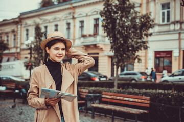Lady excited about visiting new places, holding a map in hand, weared in trendy coat and hat over...