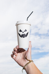holding takeaway paper cup with Halloween face in the background sky