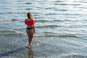 Beautiful girl in a bikini and a short blouse walking and relaxing on a sandy beach by the sea wave. Top view.