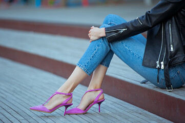 Fashionable young woman wearing high heel pink shoes, white t-shirt, blue jeans and black leather jacket. Street style.