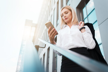 Business woman holds a jacket on her shoulder and uses a smartphone
