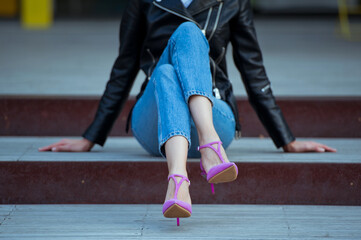 Fototapeta na wymiar Fashionable young woman wearing high heel pink shoes, white t-shirt, blue jeans and black leather jacket. Street style.