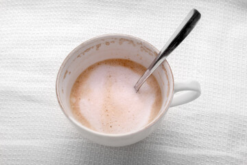 Empty half cup of latte or cappuccino coffee on white napkin, top view