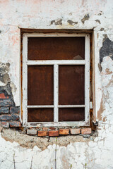 Fototapeta premium The ragged wall of an old abandoned building, with a window closed by a sheet of rusty metal. The picture was taken in Russia, in the Orenburg region, in the countryside