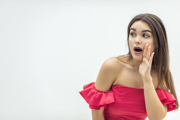 Copyspace photo of beautiful young woman in red dress, gossiping, keeping hand near mouth over white background.