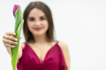 Shot of young girl wearing maroon dress and looking like tulip flower she holds in hand over white background.