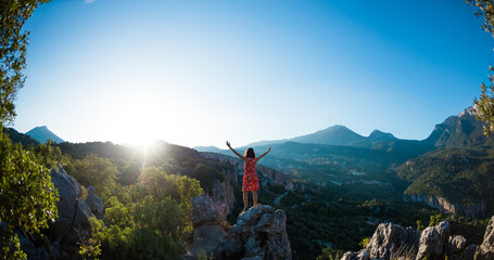 A girl in a dress stands on top of a mountain, a woman looks at a mountain valley