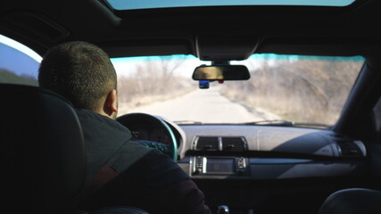 View from backseat on young man drives a car on empty road. Guy rides in his modern SUV through countryside. Male tourist travels on his auto. Concept of journey. Close up Slow motion