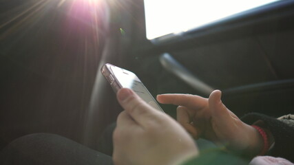 Female hands of small girl browses social media on smart phone during riding on modern SUV. Little child sits in backseat of moving car and types text message on her mobile phone. Slow motion